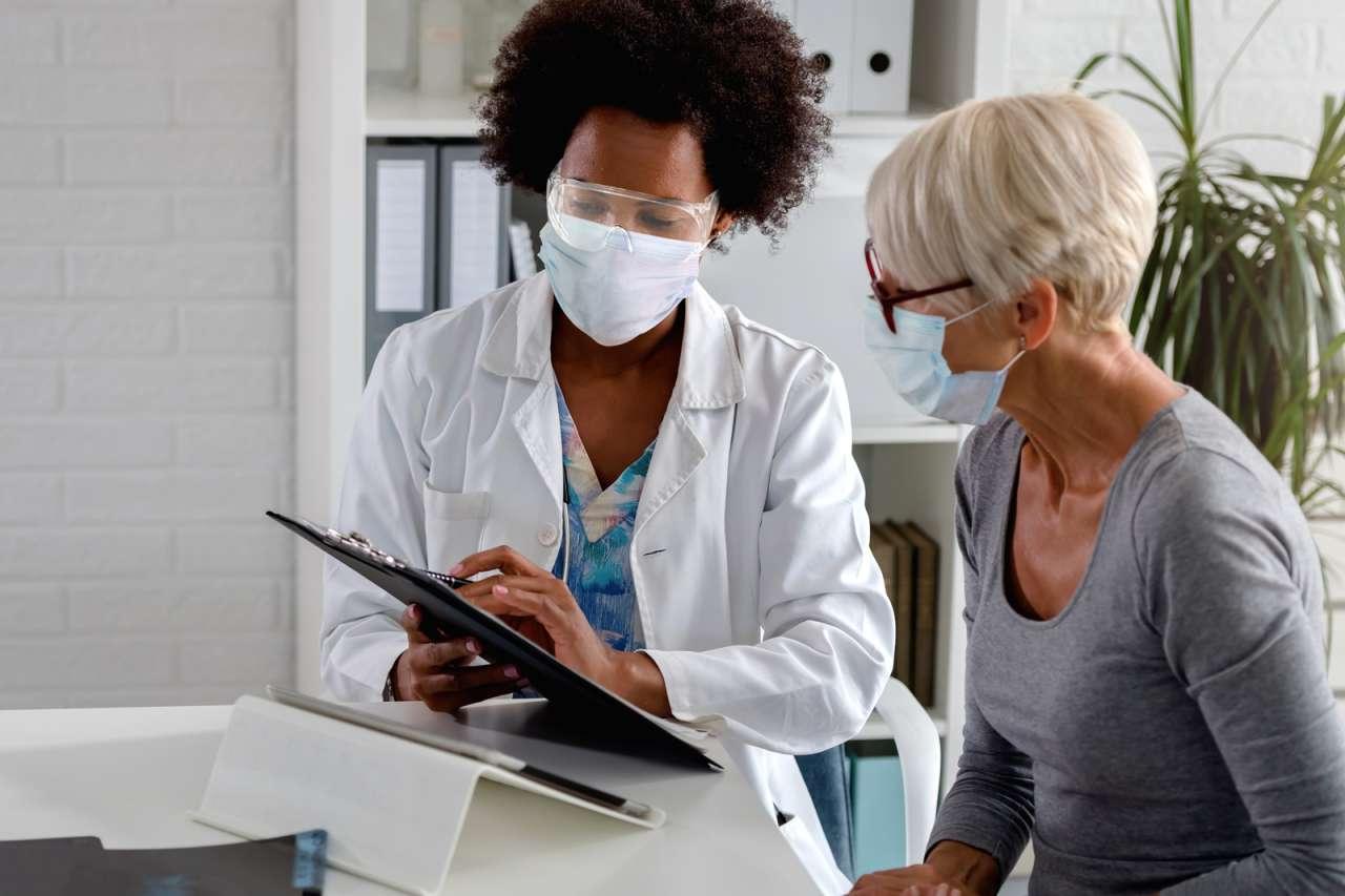 A black doctor with mask and face shield showing documents to a patient.